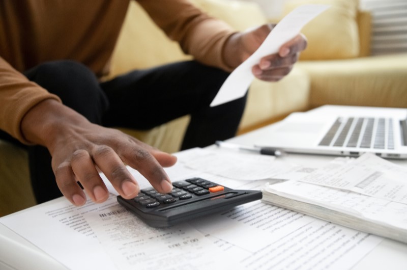 Mantenha um controle constante das contas | Foto de uma pessoa segurando uma conta e usando a calculadora | Dúvidas sobre dívidas | Eu Dou Conta 
